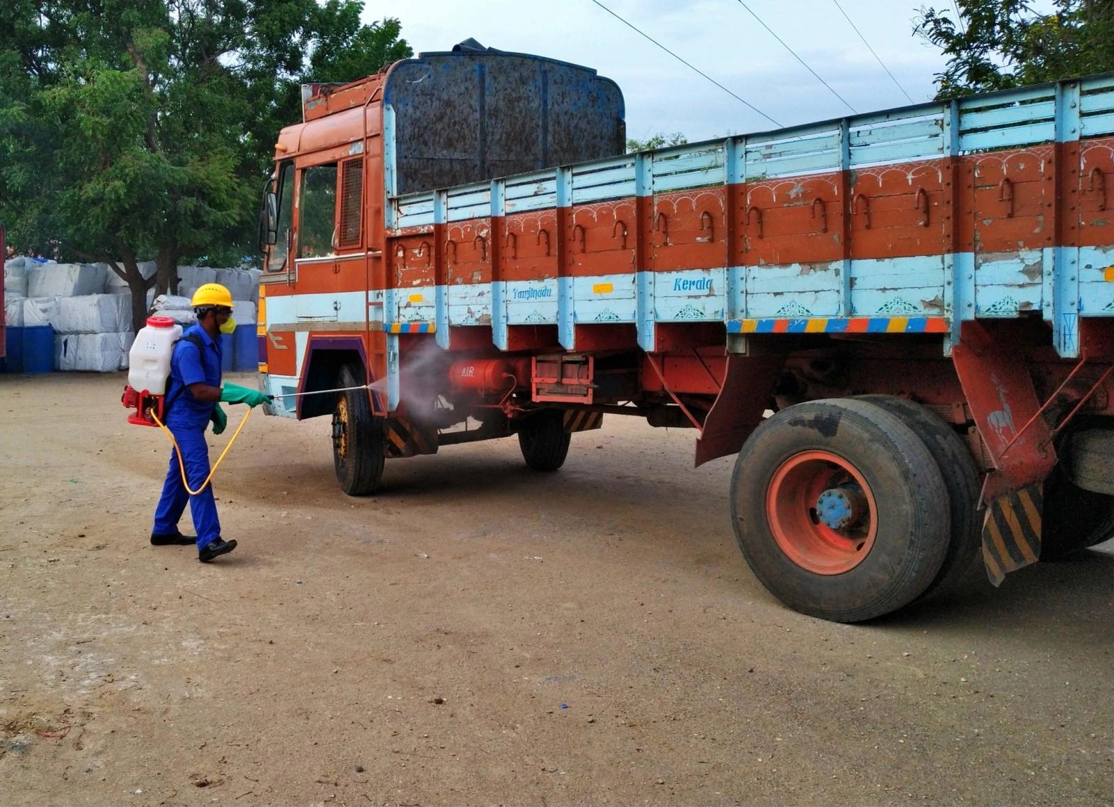 Worker using a backpack sprayer beside a delivery truck.