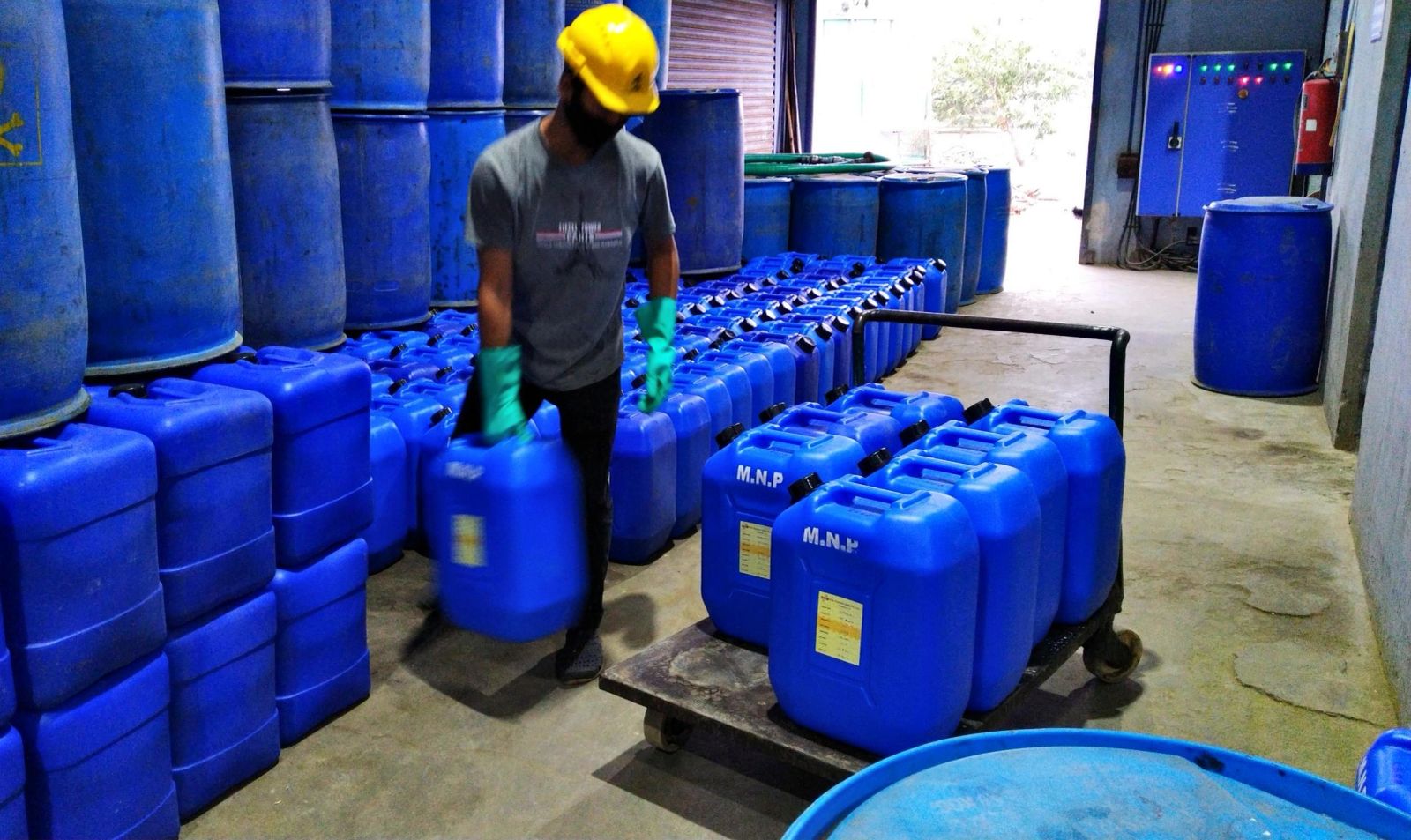 Worker moving a blue M.N.P container among rows of stored containers.