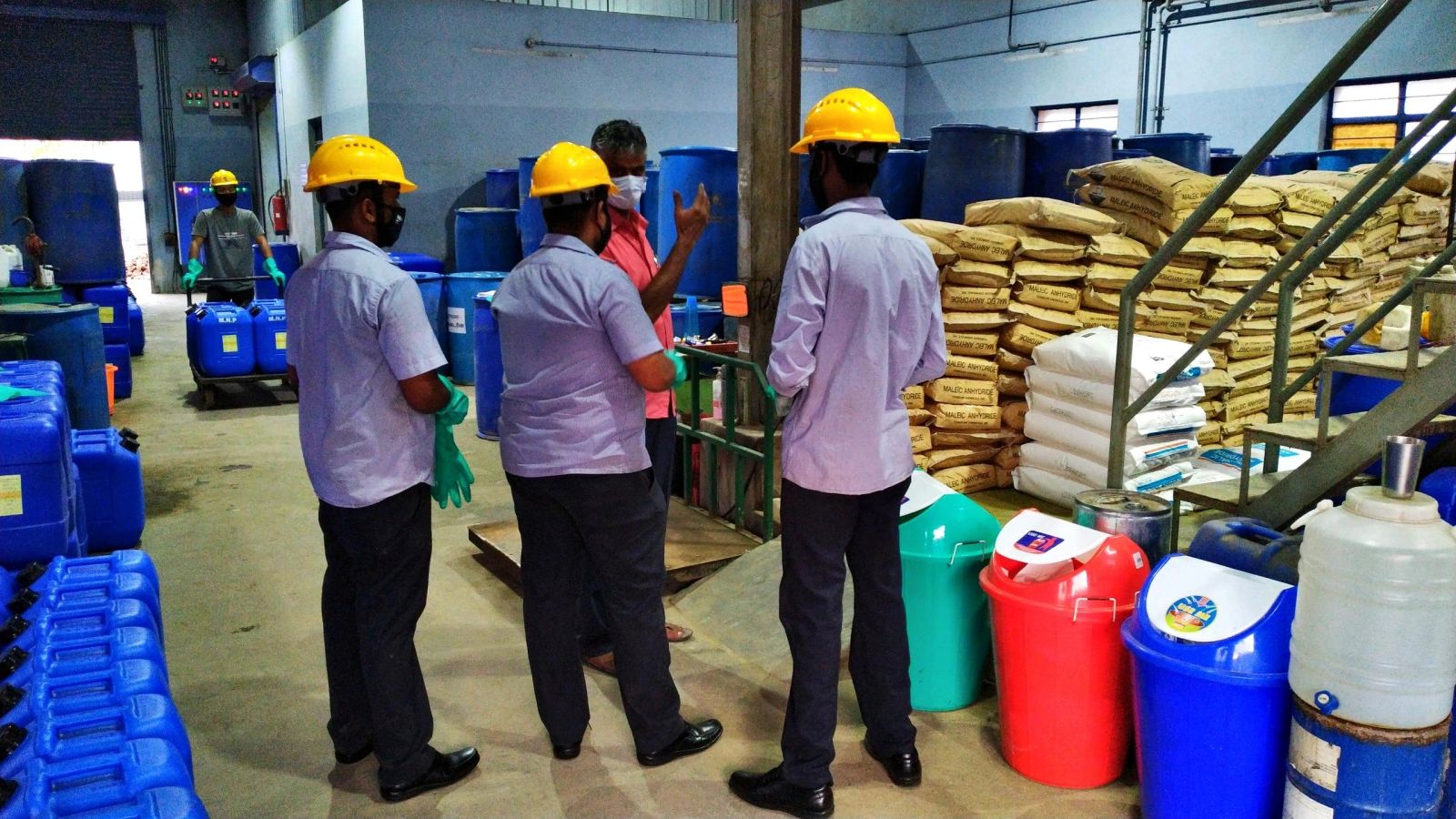 Factory staff beside blue containers, raw-material bags, and color-coded bins.