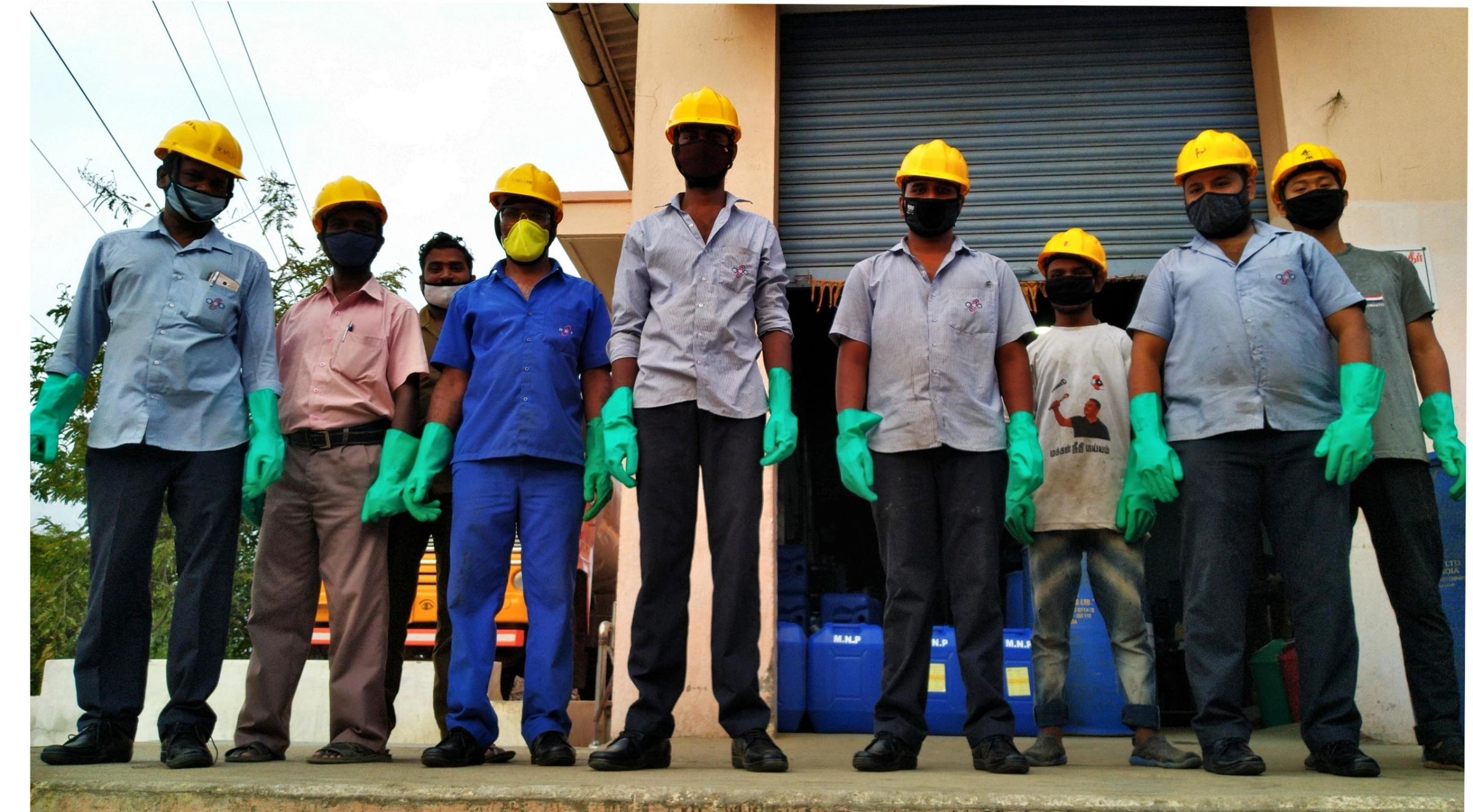 Factory staff wearing hard hats, masks and gloves outside the facility.