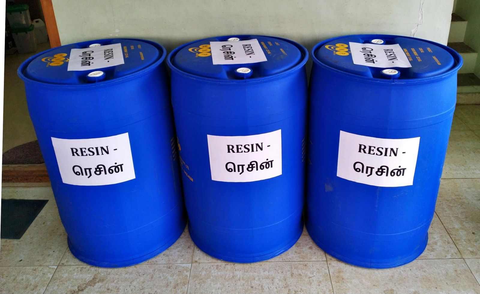 Three blue resin drums labelled “RESIN” in English and Tamil.